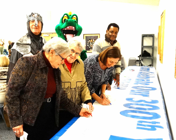 Signing the commemorative banner of St. George's tricentennial year are in front (l-r) Helen Abrams, Carol Wells, Carol Lewis, and Stuart Burgh. In back are St. George (Dan Reed) and the dragon (Jim Brand).